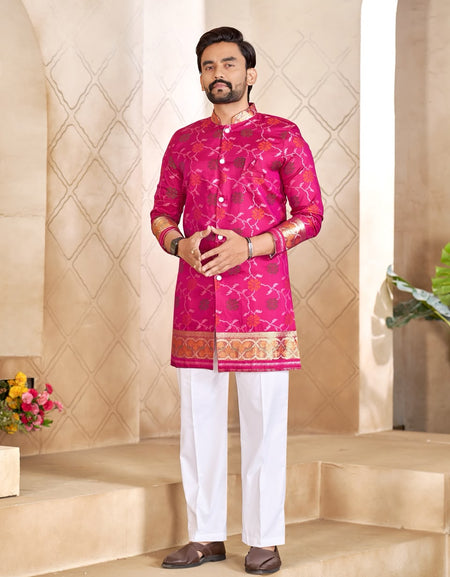 A man modeling a bright pink Indian ethnic kurta with gold and silver embroidery, paired with white trousers and brown sandals, standing on beige stone steps.