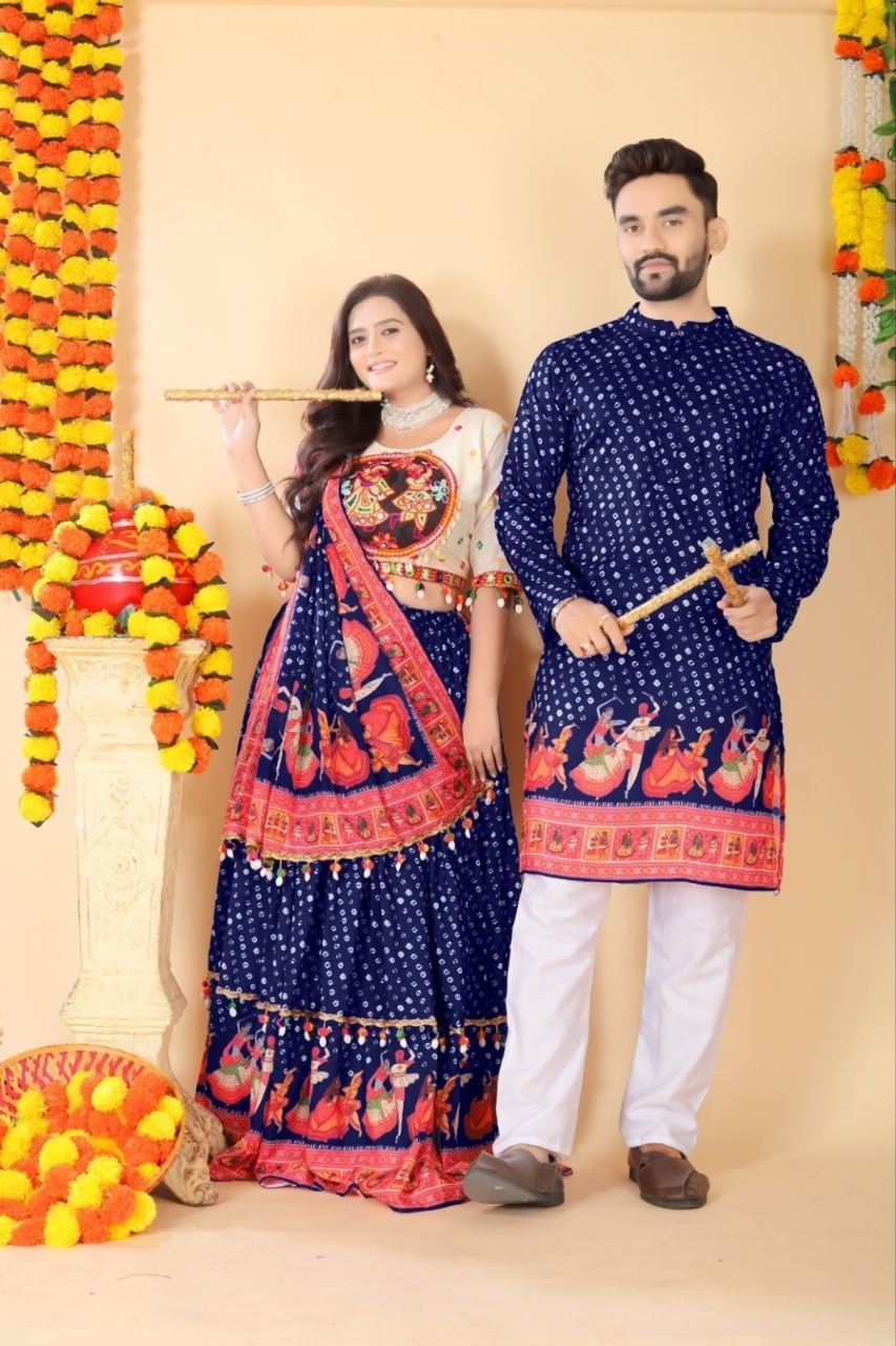 A man and a woman posing in traditional Indian attire. The woman wears a navy blue and red lehenga choli with intricate embroidery, and the man wears a matching navy blue kurta with red borders and white pants.