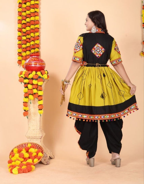 Load image into Gallery viewer, A woman modeling a traditional Indian salwar kameez outfit from the back, featuring a mustard yellow and black kurta with colorful embroidery, paired with black salwar pants, set against a beige background decorated with marigold garlands.
