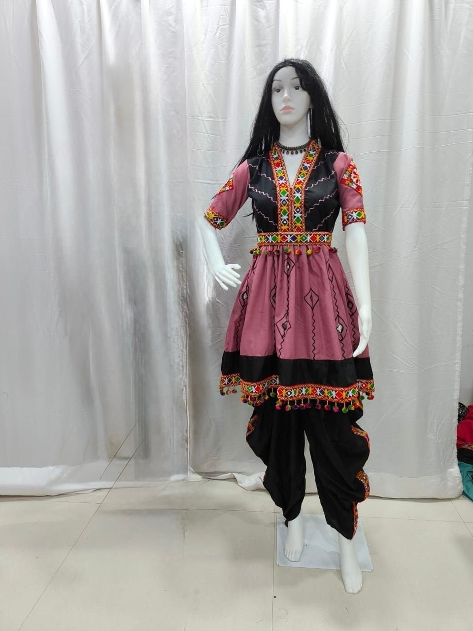 A traditional women's Navratri Garba outfit displayed on a mannequin, featuring a dusty pink kurta with black and multicolor geometric embroidery, paired with black pants.