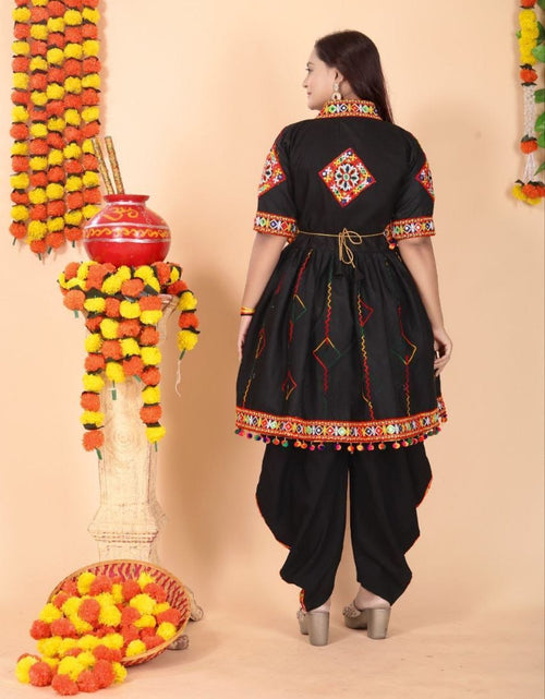 Load image into Gallery viewer, A woman wearing a black traditional Indian outfit with colorful embroidered details on the sleeves, hem, and back, standing in front of a beige backdrop decorated with marigold garlands and a red pot.
